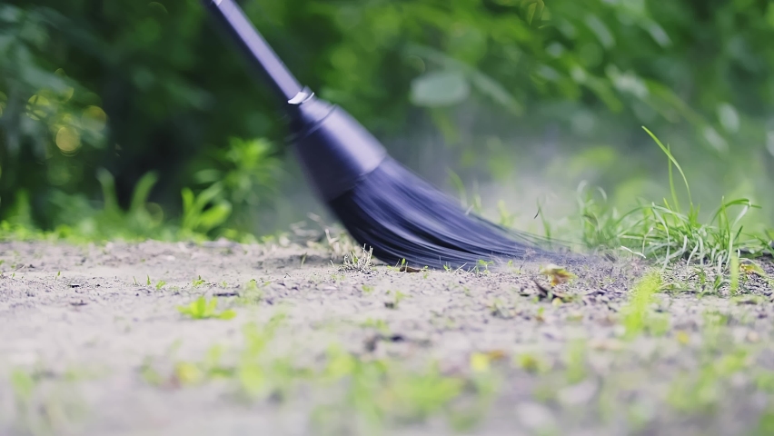 Garden chores. Footage of a broom sweeping the ground in the garden with green leaves as a background with black broom. High quality 4k footage
