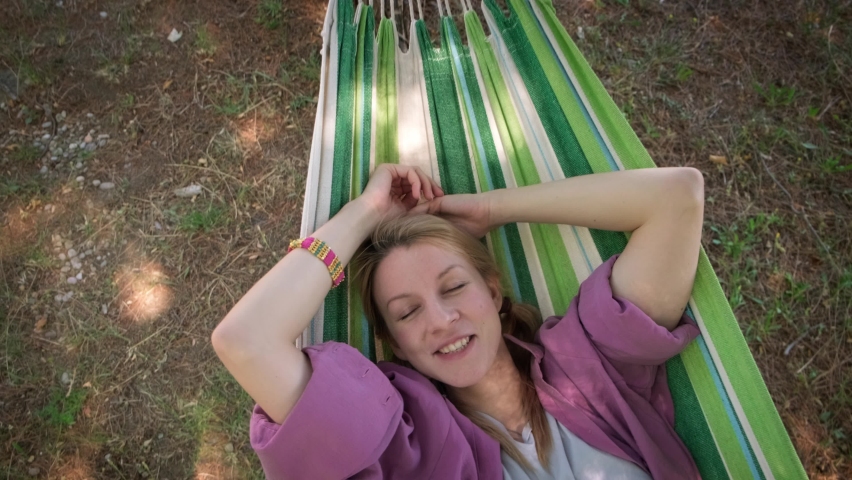 Happy young woman lying and swinging in hammock and smiling, top down shot.