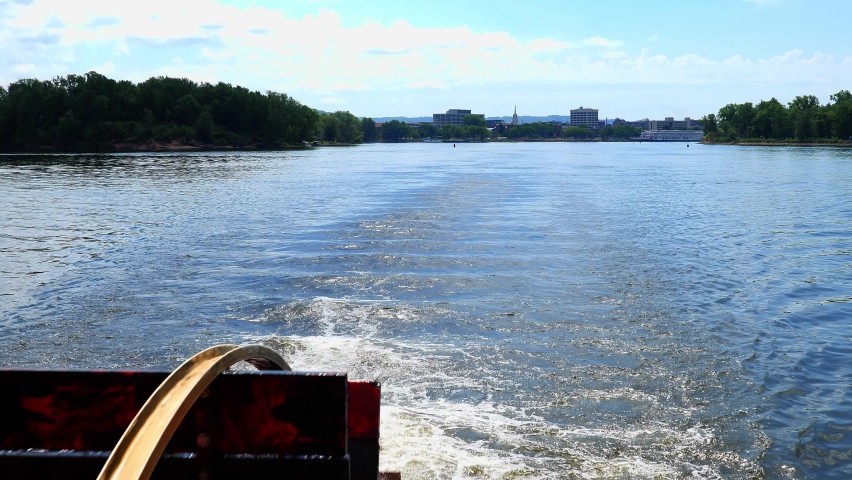 Red Wooden Paddle-wheel turning and causing foamy Mississippi River water, with La Crosse, Wisconsin in the distance.