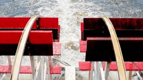 Closeup of the red rotating paddle wheels of a cruise boat in motion on the water, with tilt up to view of La Crosse, Wisconsin, in handleld clip.