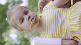 VERTICAL VIDEO: Little girl eats a colorful gingerbread and holds a milkshake in her hand. Close-up portrait of cute child girl sitting on park bench and eating cookies with a milkshake.
