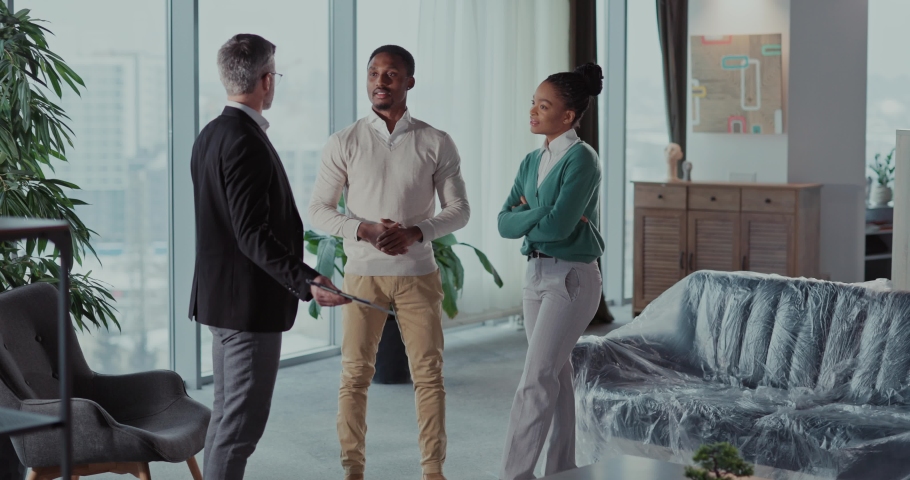 Real estate agent in formal suit talking to african young couple making agreement signing contract for purchasing new home. Apartment interior. Communication. Royalty-Free Stock Footage #1092829497