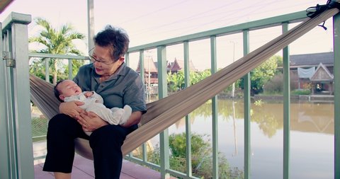 portrait happy Asian person generation family senior woman grandmother holding cute newborn baby infant child and care with love sitting on swing together at home, grandparent smiling embracing babyの動画素材