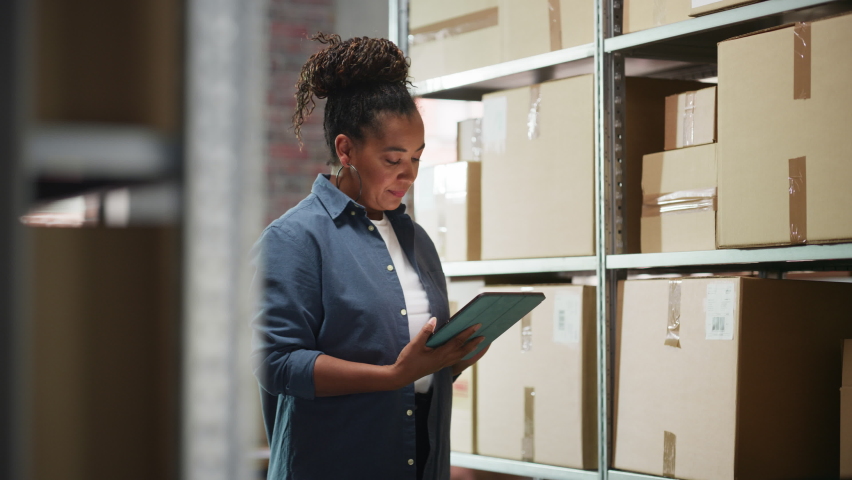 Portrait of a Successful Employee Checking Inventory, Writing in Tablet Computer. Black Woman Posing for Camera and Smiling in a Warehouse Storeroom with Orders Ready for Shipment. Royalty-Free Stock Footage #1092830151