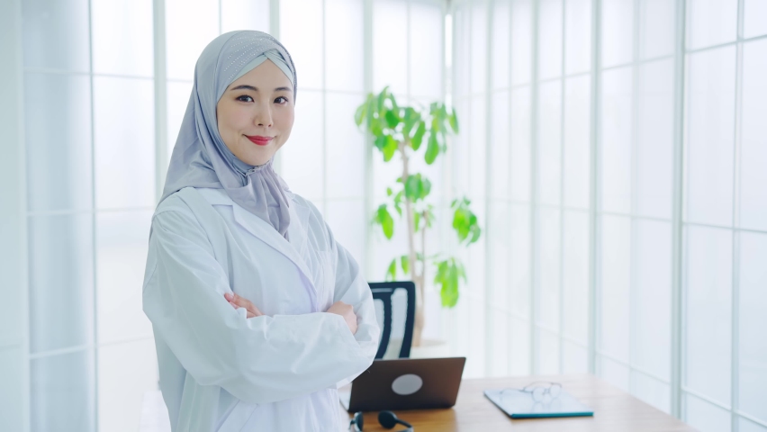 Asian woman in a lab coat wearing a hijab standing in the office.
