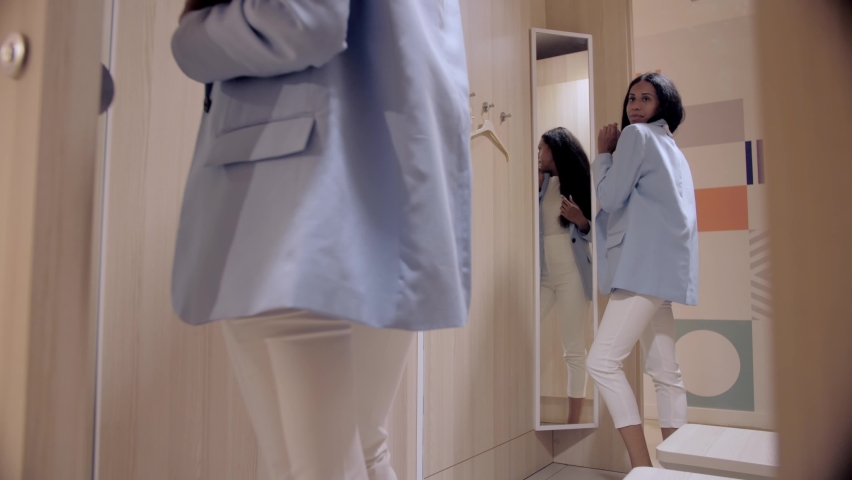 African American woman in the fitting room trying on clothes from the store. Black woman buying clothes.Woman trying on clothes in the store.Girl in a blue jacket looking in the mirror Royalty-Free Stock Footage #1092834767