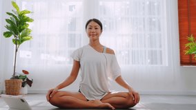 Beautiful asian woman in comfortable sportswear practicing yoga on mat strong stretching to exercise at home. female body muscle and  training fitness indoors. Healthcare yoga therapy and sports.