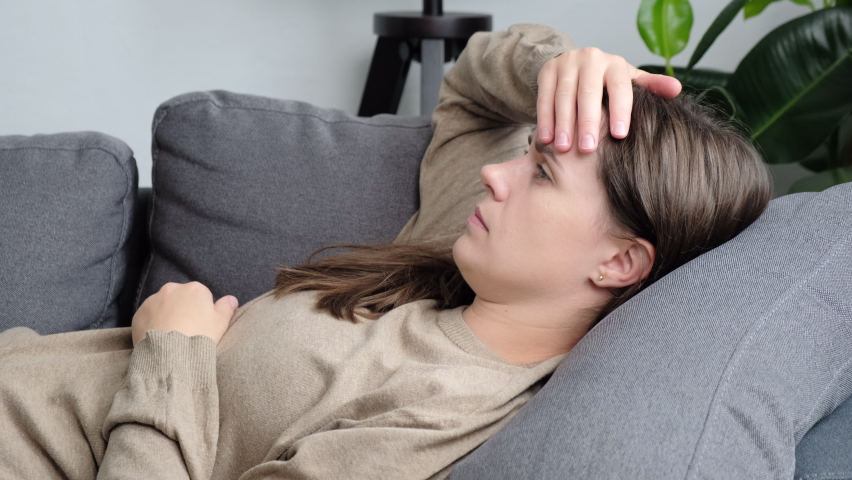 Close up of anxious young woman lying on grey sofa, feeling doubtful making difficult decision. Nervous caucasian female suffering from negative thoughts, unwanted pregnancy, relationship problems | Shutterstock HD Video #1092838169