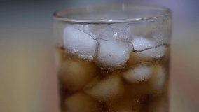 Pouring Cola with ice cubes close-up. Cola with Ice and bubbles in glass. Coke Soda closeup. Food background. Rotate glass of Cola fizzy drink over brown background.