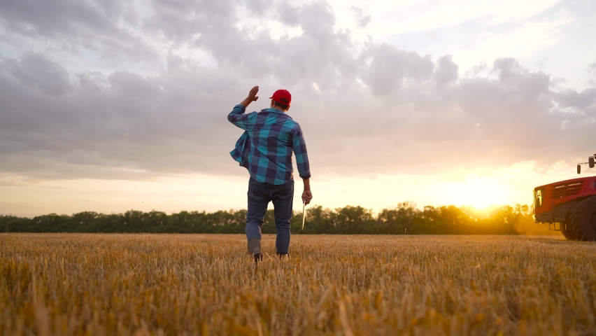 Agriculture. Working farmer walks with tablet across field against background of tractor. A worker on tractor cultivates and fertilizes field. Farmer controls operation of tractor in the wheat field. Royalty-Free Stock Footage #1092839707
