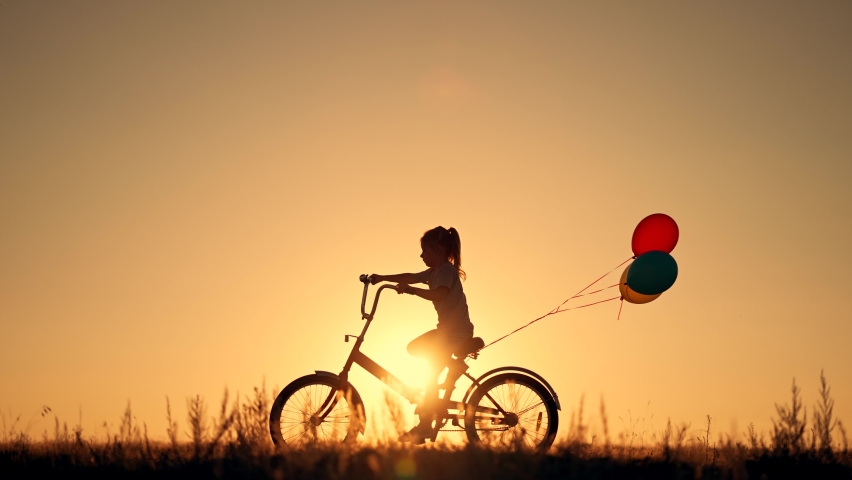 Dream kid. Silhouette of kid on bike in park. Girl rides in park on green grass. Child games in nature.Traveling with balloons on bike.Active child freedom in summer.Girl learns to ride bike in nature Royalty-Free Stock Footage #1092839717