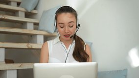 Young woman in headset conducts online conference sharing useful knowledge. Female mentor uses laptop for communication sitting on stairs closeup