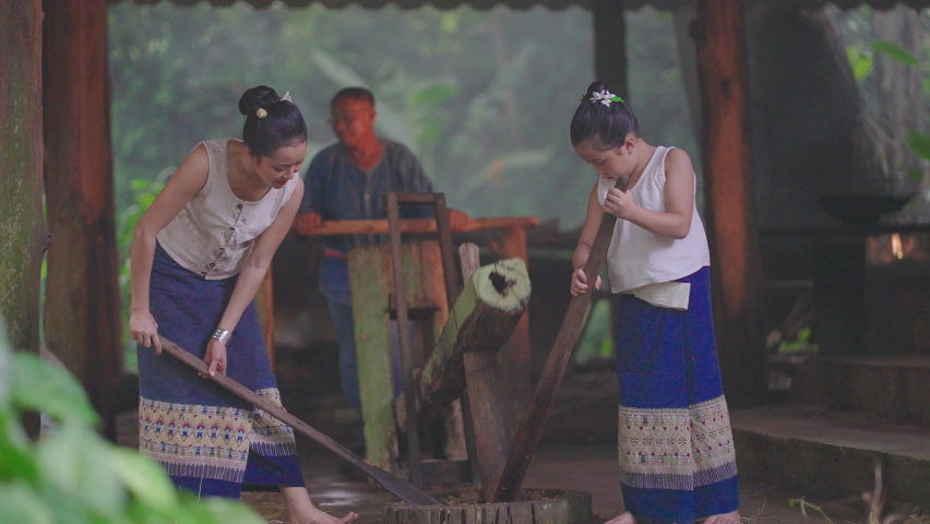 Asian mother and daughter with Thai tradditional clothes help to puncture or smash pieces of vegetable and herb to make food for elephant. They look enjoy good activities together.