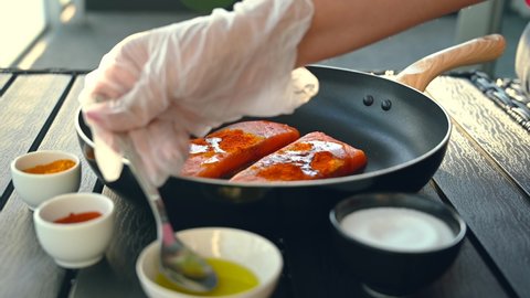 The red salmon fish is being marinated by turmeric, salt and pepper by baby hand in a black pan. 4K video
