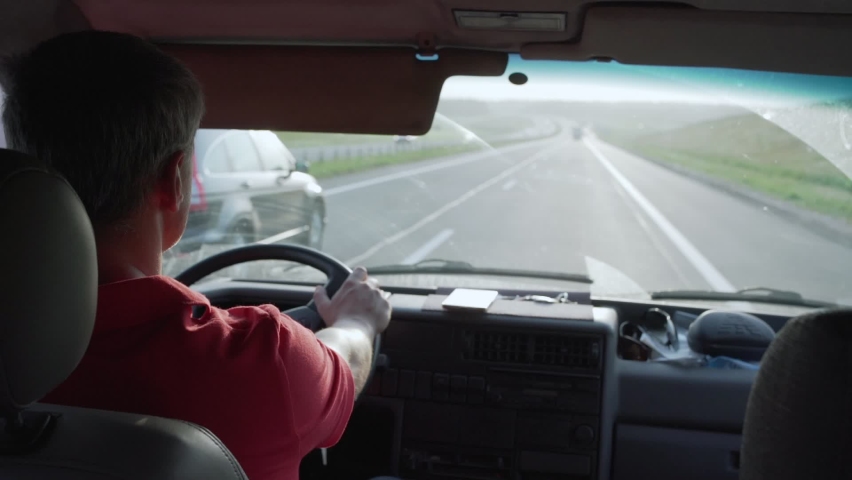 concentrated man with short gray hair in red shirt in summer while driving car on highway