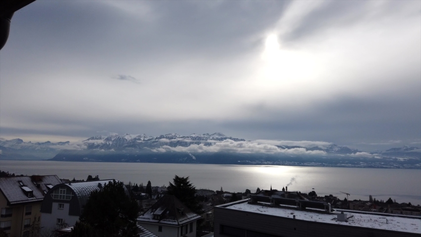 Moving timelapse; cloudy day over the geneva lake during the winter, snowy french mountains behind