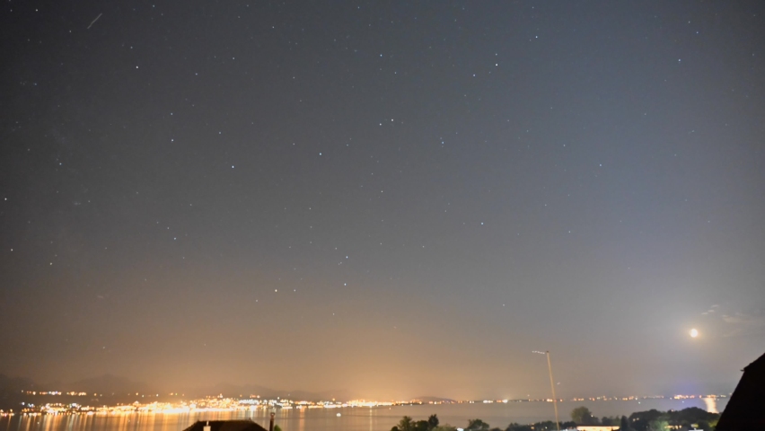 Starry night above Lake Geneva, the sky is moving and the lights of the cities of Evian and Lausanne create a halo of light, timelapse