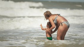 Cheerful happy caring mom throws her little funny son up over the calm blue sea on a warm summer sunny vacation under the warm sun. 4K UHD slow-mo video
