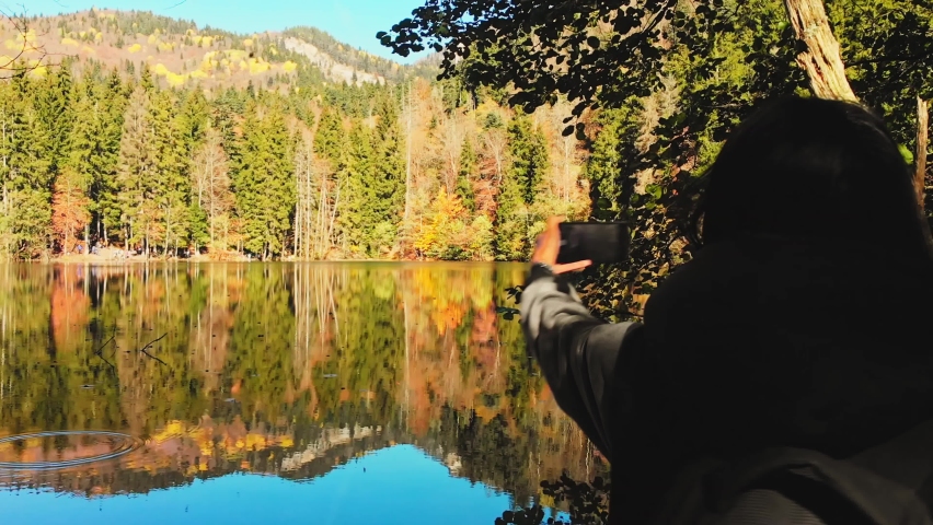 Close up caucasian woman standing by lake taking panoramic photo of scenic autumn nature outdoors