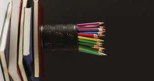 Vertical video of stack of books, crayons and lying on black background. School equipment, tools, learning and education concept.