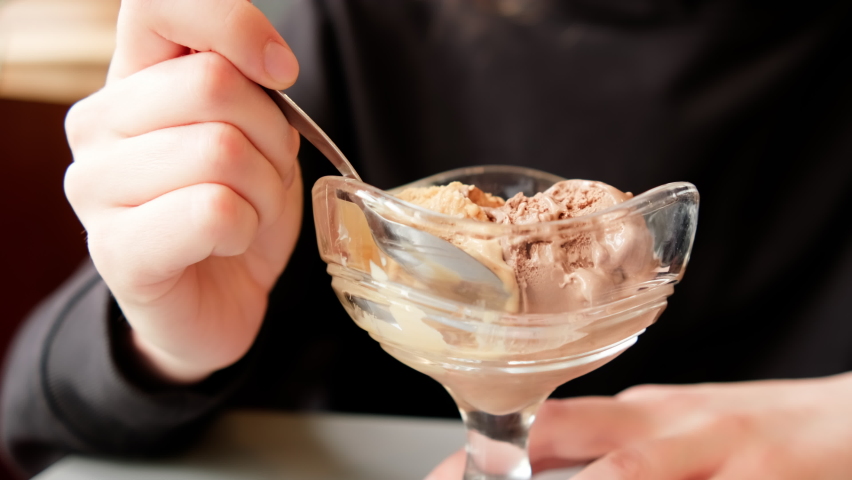 Eating ice cream in cafe. Young woman with a spoon savouring chocolate ice cream from sundae glass cup. Handheld close up shot Royalty-Free Stock Footage #1092868265