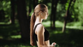 a beautiful girl is engaged in sports in the park, lifting the fitness dumbbell