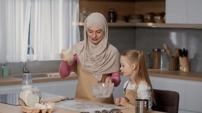 Culinary lesson at home. Happy loving muslim mother wearing hijab cooking bakery with her little daughter, kneading dough together at kitchen, slow motion, free space