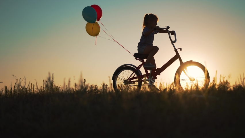 Dream kid in nature. Silhouette of child on bicycle plays in park. girl rides through natural green park with balloons. Play with balloons on bike. girl dreams of learning to ride bike in nature. Royalty-Free Stock Footage #1092872723
