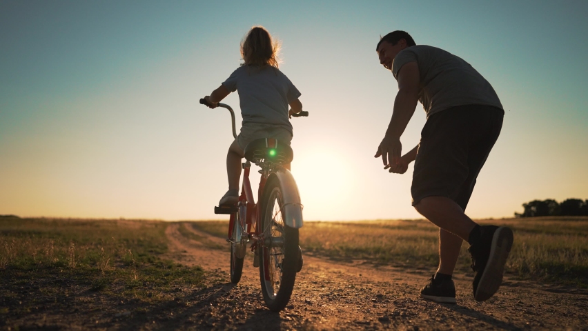 Happy family. Father teaches daughter to ride bike in park. father helps his daughter in her studies. happy child dreams of traveling by bike. child is learning to ride bike. Royalty-Free Stock Footage #1092872725