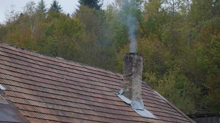 Smoke coming out of the chimney. Autumn forest on background. Atmosphere of comfort, warmth and safety. Comfortable house. Video 4k. Ukraine, fall season