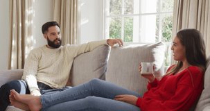 Video of happy caucasian couple siting on sofa and drinking coffee. Domestic lifestyle and leisure at home.