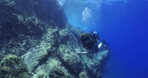  scuba diver exploring around a reef underwater deep blue water big rocks and bubbles ocean scenery