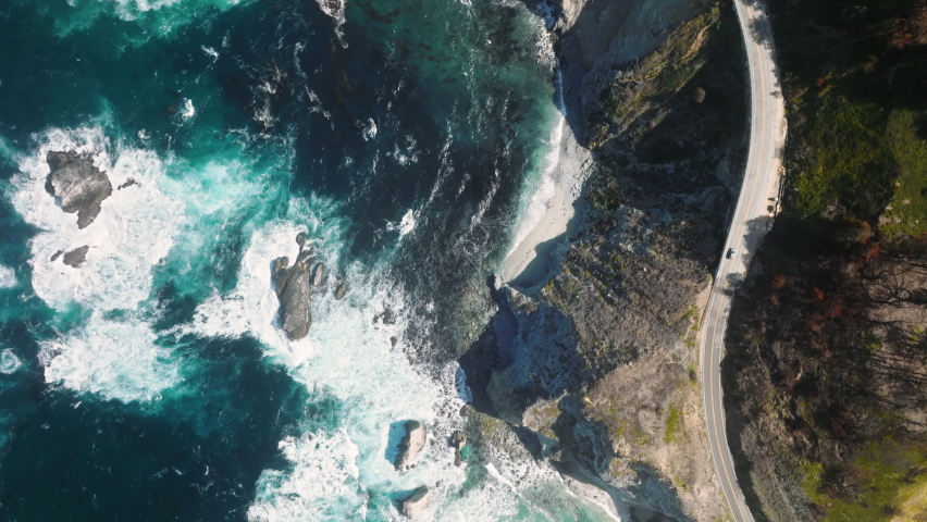 Aerial view of car driving by cinematic rocky ocean coast. Beautiful mountain road with scenic ocean view. Driving on mountain road. Road trip. Rocky Mountain landscape Car driving by Big Sur coast Royalty-Free Stock Footage #1092882839