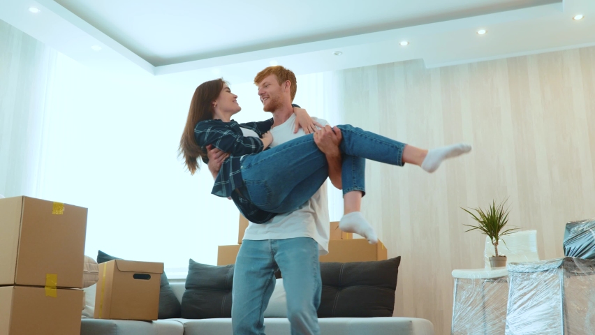 Joyful married couple feeling happy together in new house. Low angle view. Loving young husband spinning his beloved beautiful wife on hands in new apartment. Own place. Moving day Royalty-Free Stock Footage #1092900283