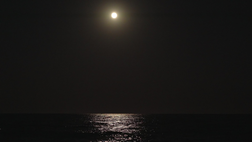 A large full moon illuminates the ocean. Waves, light on the water.