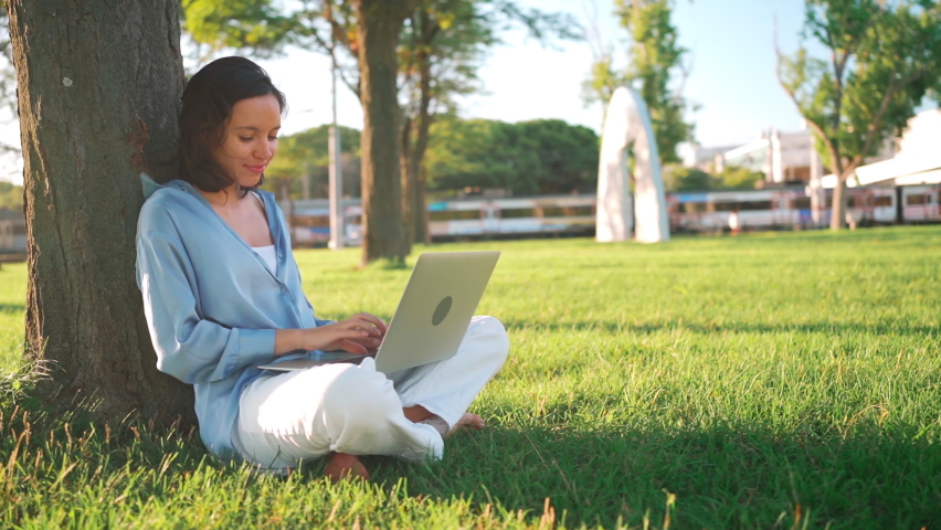 Happy brunette woman using laptop computer in park. Young female freelancer working outdoors in city park. Caucasian businesswoman at remote work. Business person female. New normal remote work  | Shutterstock HD Video #1092903865