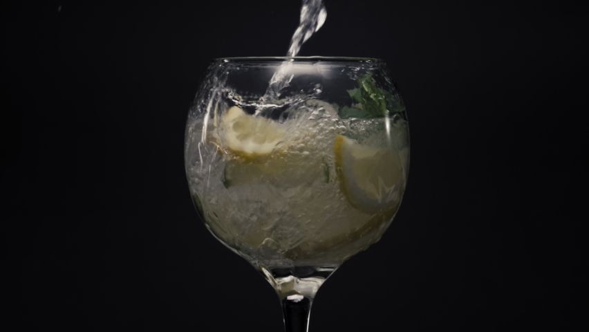 Bubbled lemon ice mint deink closeup. Fresh water jet pour on ice herbs and lime in wineglass macro. Sparkling lemonade mojito cocktail black view. Tasty beverage with drop. Preparing cocktail