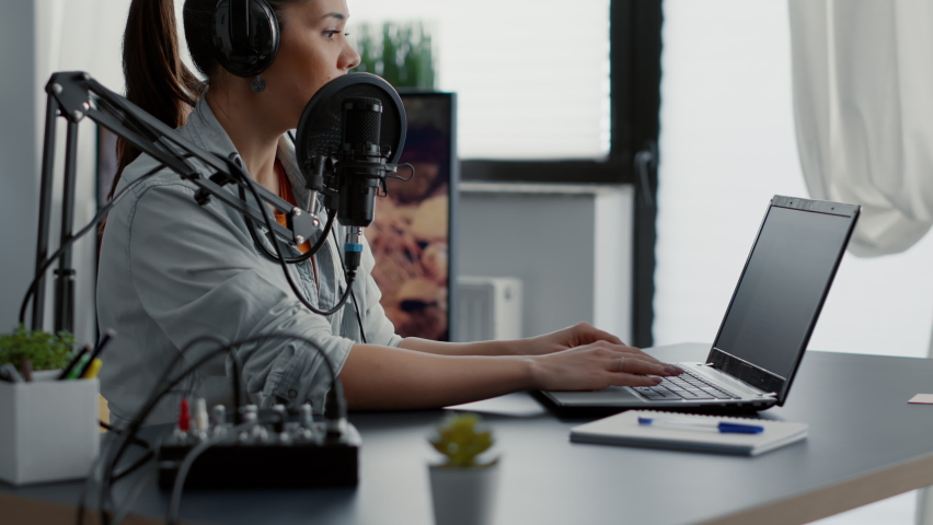 Podcast show host typing on laptop while talking to audience. Internet popular creative content creator chatting with public on live chat while speaking on modern microphone.