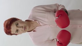 Coping with difficulties in business life. Young woman with boxing gloves isolated on white background. Young woman exercising with boxing gloves, nervously punching camera. Strong woman portrait.