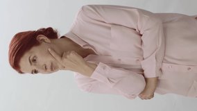 The woman thinks, looks for a new idea. Woman on a white background with hands on chin looking at empty advertising spaces to the left or right of the screen.Video for the vertical.