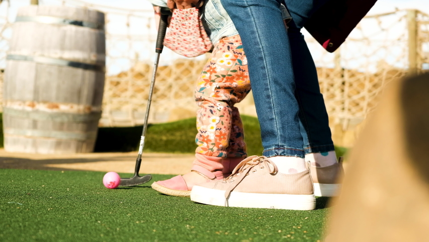 Mom assists toddler to make a putt with a pink ball at miniature golf Royalty-Free Stock Footage #1092920375