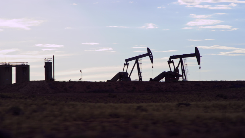 Driving by two active oil pumps in silhouette in Vernal Utah oilfield Royalty-Free Stock Footage #1092924799