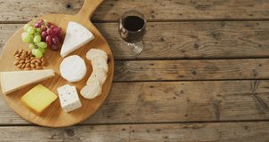Video of cheeses, bread, grapes and nuts on board and red wine on wooden table, with copy space. quality light food snack and drink.