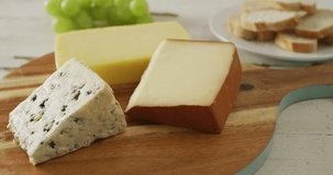 Video of assorted cheeses on chopping board, with grapes and bread on rustic wooden table. quality, tasty light food snack.