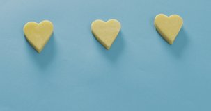 Video of row of heart shapes of cheese on blue background with copy space. savoury food, fun cheese lovers snack.