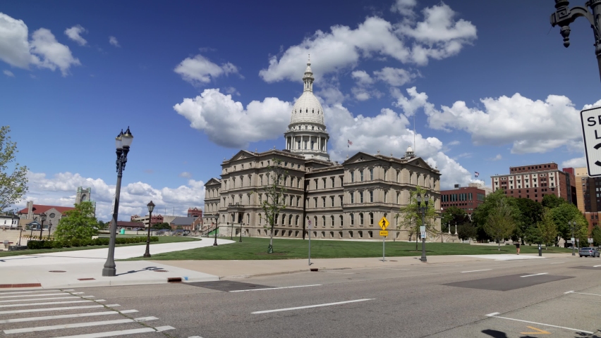 Michigan state capitol building in Lansing, Michigan with ground level time lapse video showing fast moving clouds with zoom in.