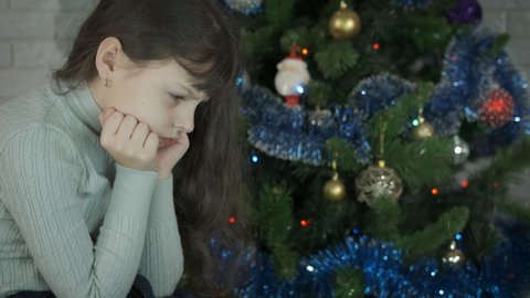 Child during lonely Christmas. An alone young girl celebrate the Christmas by the tree in the room.