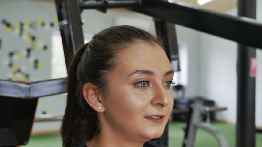 face of a beautiful smiling middle eastern woman with gray eyes and lush eyelashes exercising in the gym on a simulator lifting weights with her hands Royalty-Free Stock Footage #1092934273
