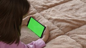 A girl of 7-8 years old uses a mobile phone with a green screen. Close-up.