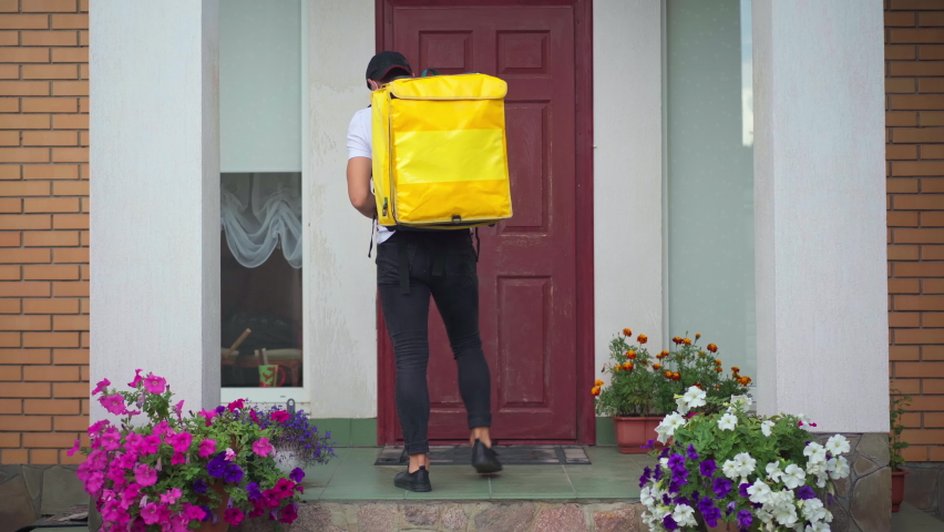 Back view courier leaving parcel at entrance knocking in door walking away. Caucasian delivery man in coronavirus face mask delivering food and drink on pandemic. Contactless service concept | Shutterstock HD Video #1092943721